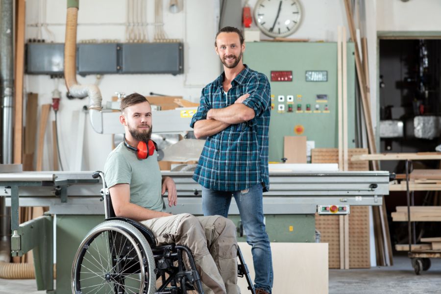 Carpenter In Wheelchair In Workshop With Colleague